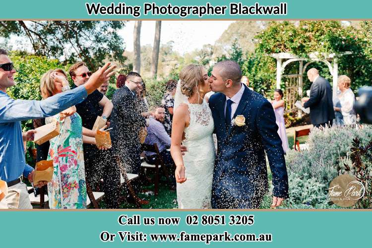 Photo of the Bride and the Groom kissing while showering rice by the visitors Blackwall NSW 2256