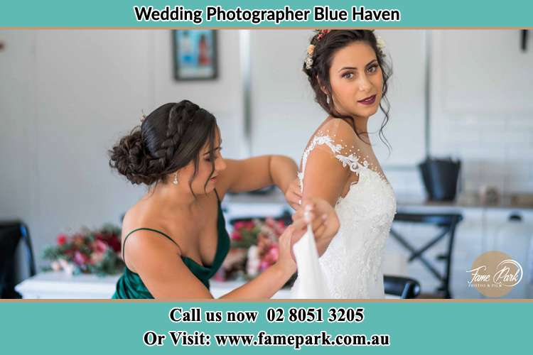 The Bride is being helped by bridesmaid trying to put her bridal gown Blue Haven