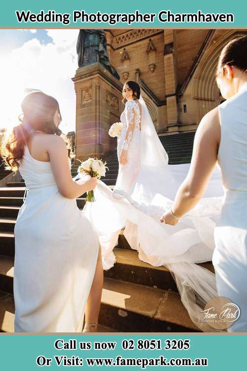 Photo of the Bride smiling to the bridesmaid holding the tail of her wedding gown at front of the church Charmhaven NSW 2263