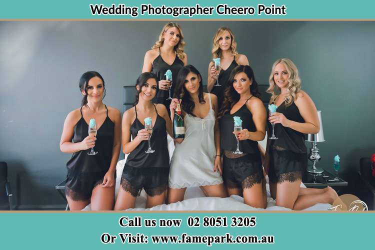 The bride holding a bottle of wine poses with the girls in front of camera Cheero Point