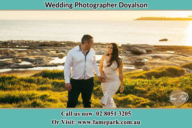 Photo of the Groom and the Bride walking near the shore as they look at each other Doyalson