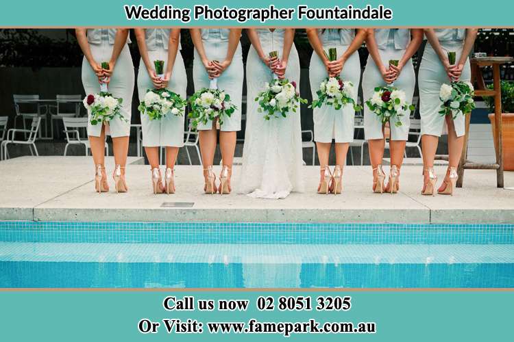 Behind photo of the Bride and the bridesmaids holding flower near the pool Fountaindale NSW 2258