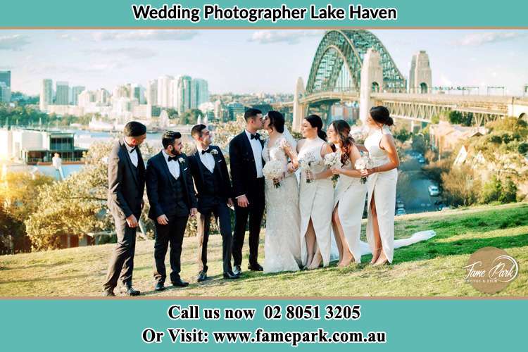 Photo of the Groom and the Bride kissing with the entourage near the bridge Lake Haven NSW 2263