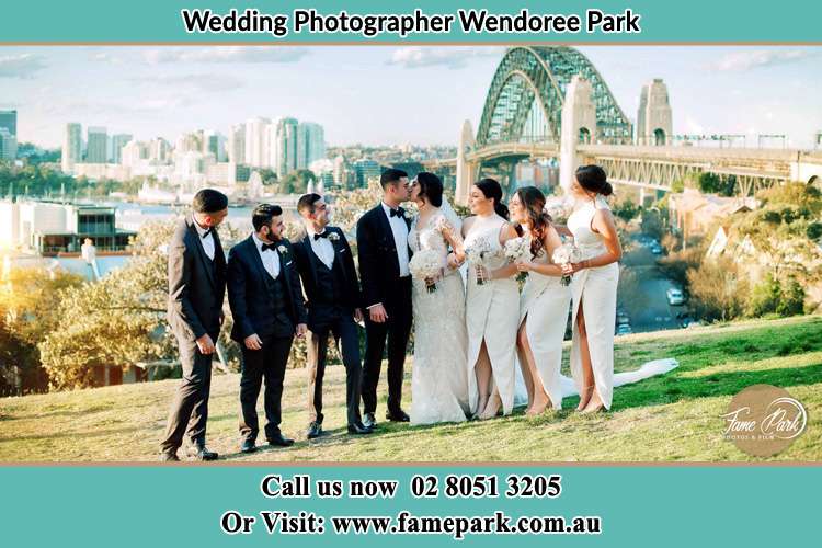 Photo of the Groom and the Bride kissing with the entourage near the bridge Wendoree Park NSW 2250