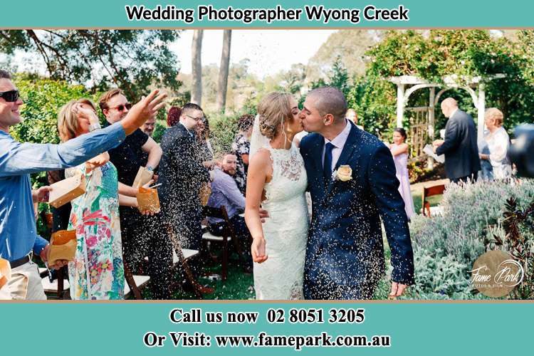 Photo of the Bride and the Groom kissing while showering rice by the visitors Wyong Creek NSW 2259